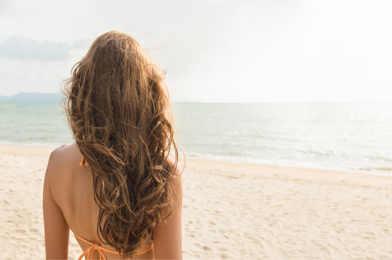 Woman with long hair sitting on a beach facing the ocean